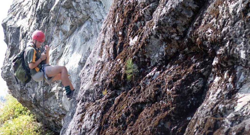 a student pauses to look down while rock climbing on an outward bound trip